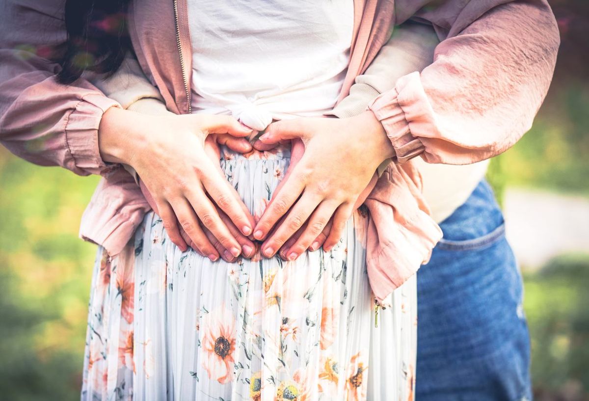 Hände formen ein Herz über dem Babybauch